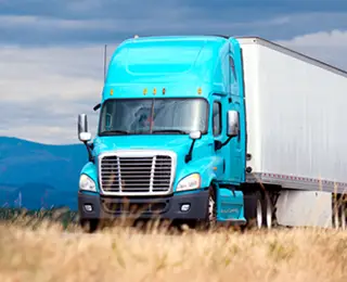 Blue semi-truck driving down the highway with dried grass on the side of road.