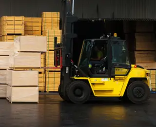 A yellow forklift moving pallets of wood in a lumber yard.