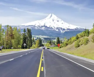 Snow covered mountain seen from a long straight road.