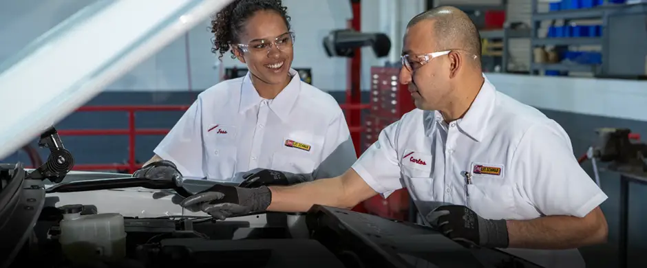 Two Les Schwab technicians inspecting a car’s battery in a garage