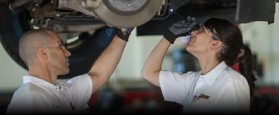 A pair of Les Schwab employees checking a vehicle's breaks while it sits on a post lift