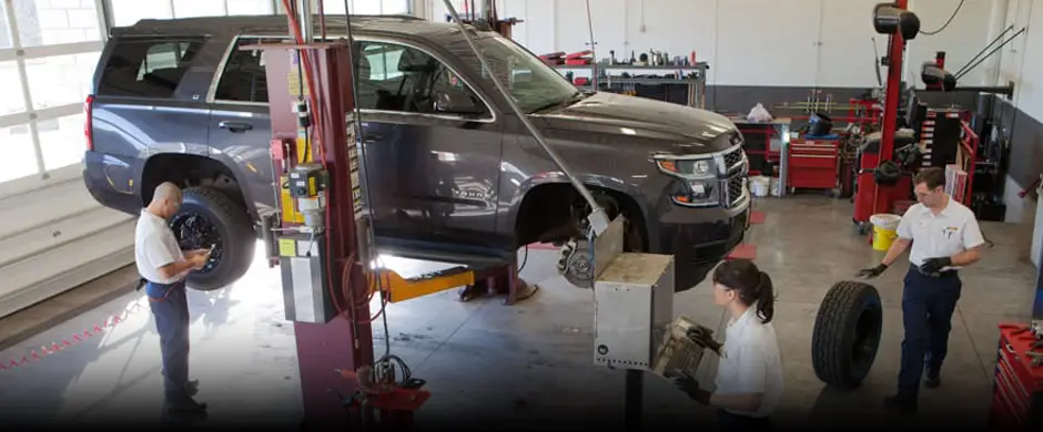 Two Les Schwab technicians working inside a garage bay, next to an SUV on a lift.